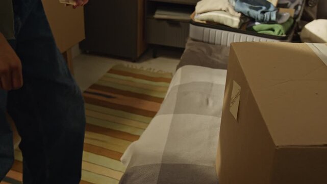 Handheld shot of African American teenager sticking sticky note labeled Done on cardboard box and walking away. Ideal for relocation services, moving companies, and real estate marketing campaigns