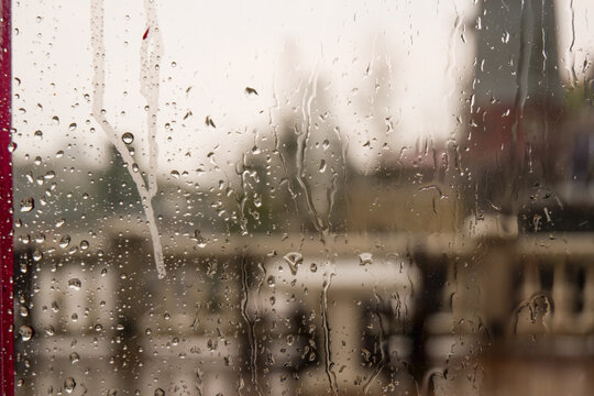 Raindrops trickle down the glass,Water Droplets on a pane of glass with blurred city background,View from a window showing rain falling rainy day,Copy space.