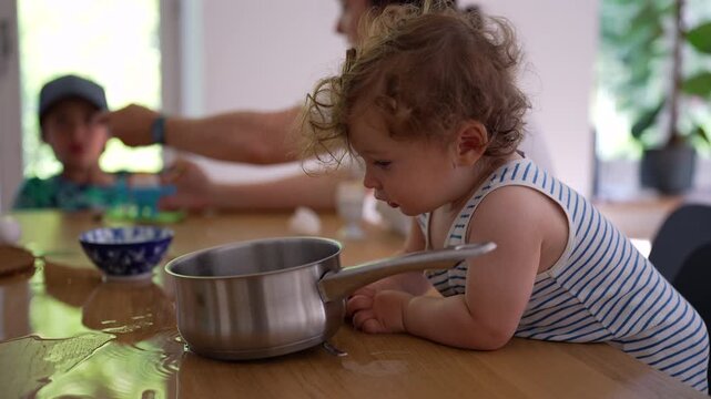 Toddler making mess with saucepan on kitchen table, capturing childhood curiosity, playful exploration and everyday family life