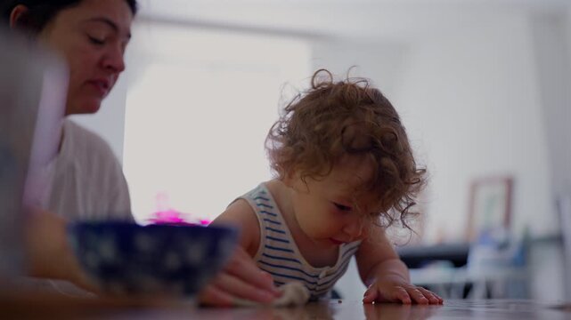 Mother cleaning spilled water with toddler watching, highlighting gentle parenting, learning by example and everyday family life
