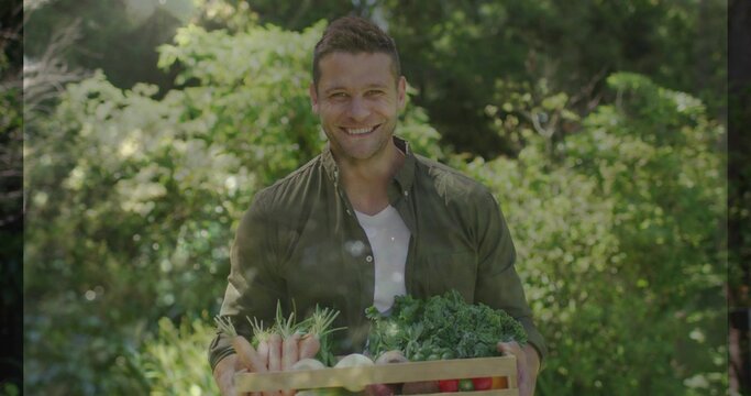 Gardener smiling down at produce holding crate in sunlit yard adjusting grip and presenting harvest