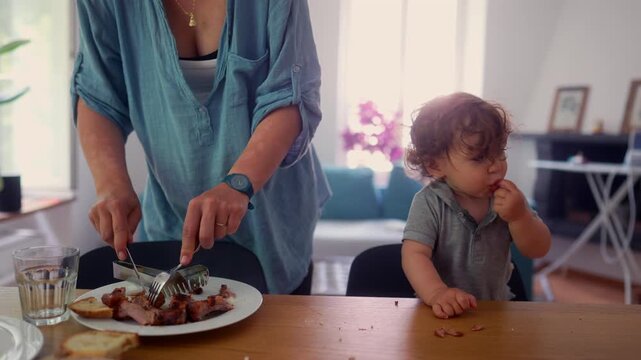 Mother serving freshly prepared meal while toddler practices self feeding, highlighting family mealtime, healthy nutrition and everyday parenting