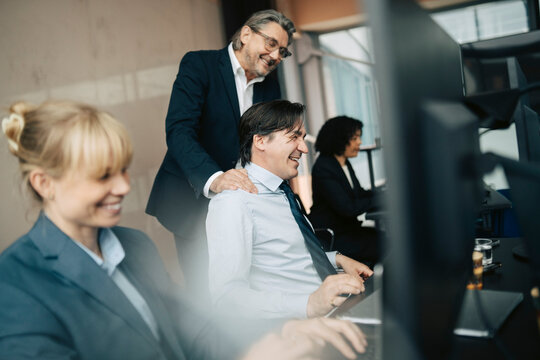 Senior manager appreciating male employee working at desk in office
