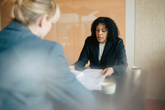Mature businesswoman discussing documents during meeting with colleague at office