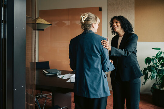 Smiling businesswoman with curly hair placing supportive hand on her colleague's shoulder