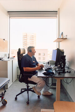 Full length of mature male physician talking on video call while sitting at desk in his cabin