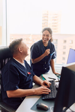 Happy male and female doctors laughing while working on computer at hospital