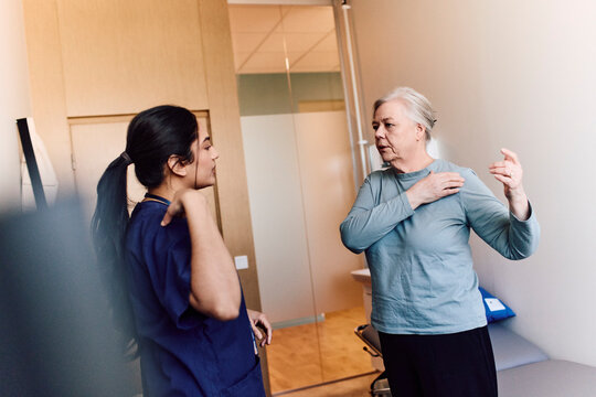 Female healthcare worker assessing senior patient's shoulder mobility during checkup