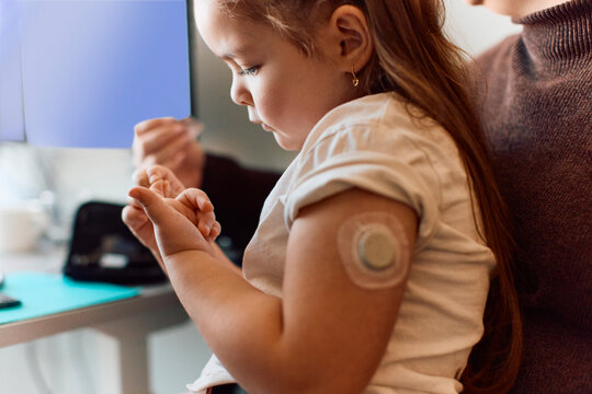 Girl sitting in doctor's clinic with blood sugar sensor attached to her shoulder