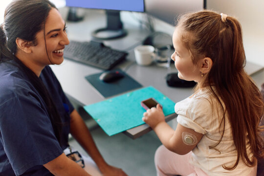 High angle view of female medical professional interacting with girl during blood sugar checkup