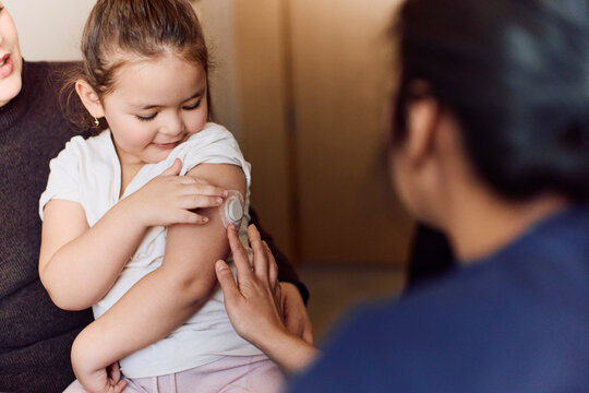 Female doctor checking continuous glucose monitor on girl's arm