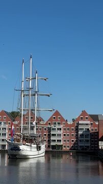 Sailing ship mast against traditional waterfront buildings in a Dutch harbor under a clear blue sky. Maritime travel footage for tourism and coastal projects.