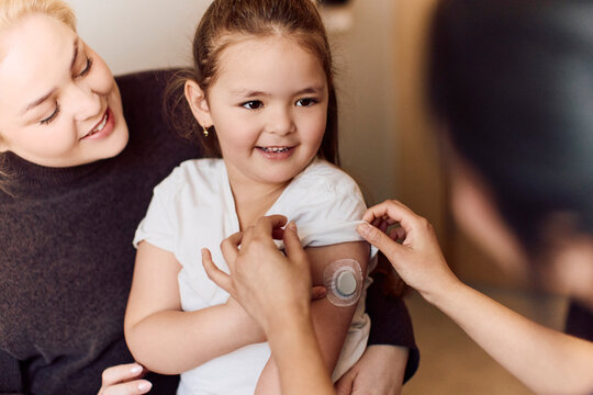 Mother with her daughter showing glucose monitor sensor to doctor during checkup
