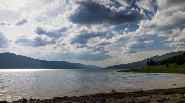 Lake with clear water and stone shore in spruce forest with fir trees against a daytime sky