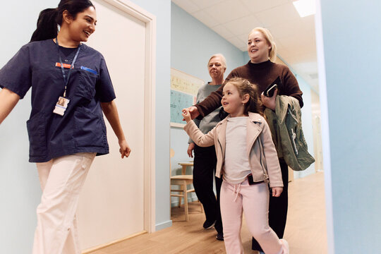 Smiling female doctor escorting girl arriving with her family for routine checkup