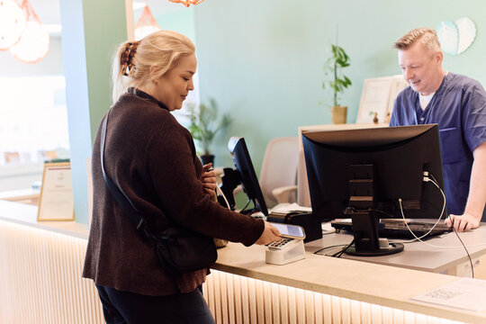 Woman using her smart phone to make contactless payment at clinic counter