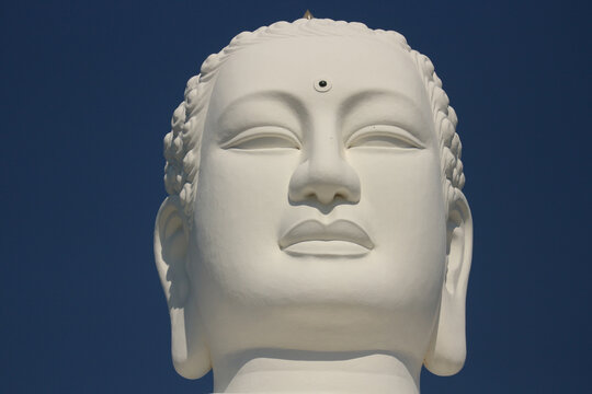 Close-up of a serene white stone Buddha statue face with closed eyes in meditation.