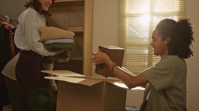 Handheld shot of African American middle aged father passing vintage speaker to teenage son packing cardboard box during family relocation. Footage ideal for moving services or real estate ads