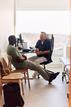Side view of young man having conversation with doctor while sitting in clinic office