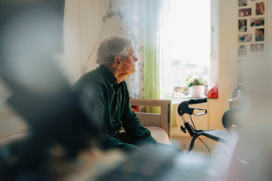 Lonely senior man contemplating while sitting on bed at retirement home