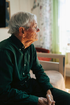 Thoughtful senior man sitting alone on bed in retirement home