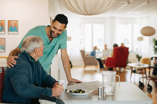 Smiling male nurse interacting with senior man sitting at table in retirement home