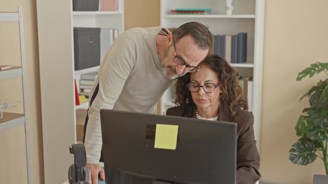 Man leaning over woman at computer with hand on shoulder and pointing at screen in office building; workplace harassment discomfort.