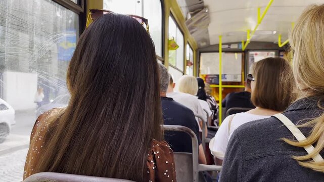 Vintage tram riding with passengers along urban streets. The sunlight highlights the interior and people, capturing the atmosphere of a busy urban commute and the daily rhythm of city life. Slow mo