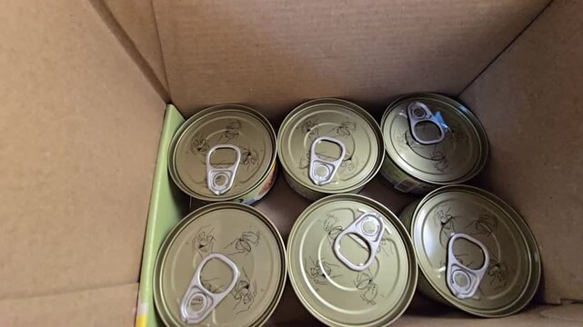 Top-down view of several sealed food cans with pull-tab lids inside a cardboard box.