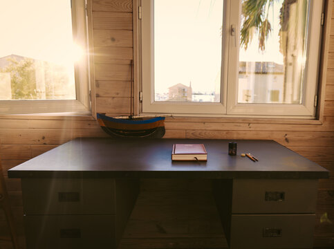 Schreibtisch unterm Fenster, mit einem Buch und ein paar Schreibuntensilien in der langsam untergehenden Sonne
