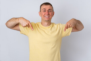 Fototapeta premium Cheerful adult man standing proudly in a yellow t shirt, smiling while pointing both index fingers down, indicating a space for important advertising content