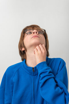 Young person with glasses wearing a blue sweatshirt, looking up with a thoughtful expression, scratching chin while contemplating new ideas or solutions