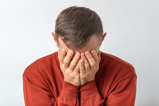 Man covering face with hands, expressing intense emotions of sadness, stress, and disappointment on a plain background, creating a powerful depiction of mental health struggles