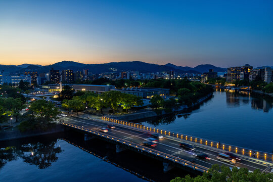 view of the motoyasu river with the illuminated peace bridge and the park at sunset during the blue hour