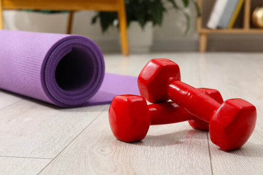 Fitness mat and red dumbbells on floor indoors, closeup