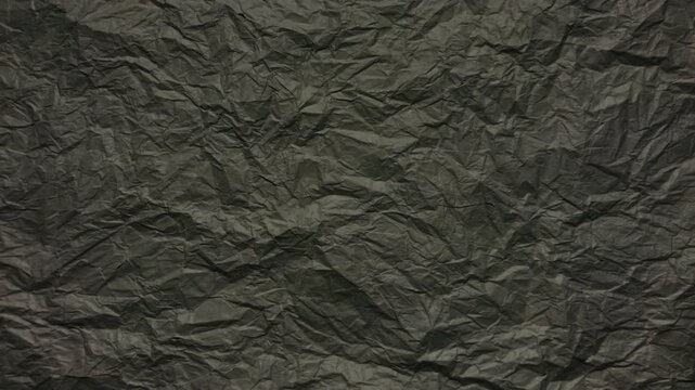 crumpled black paper texture shifts subtly under soft studio lighting creating a dramatic abstract background