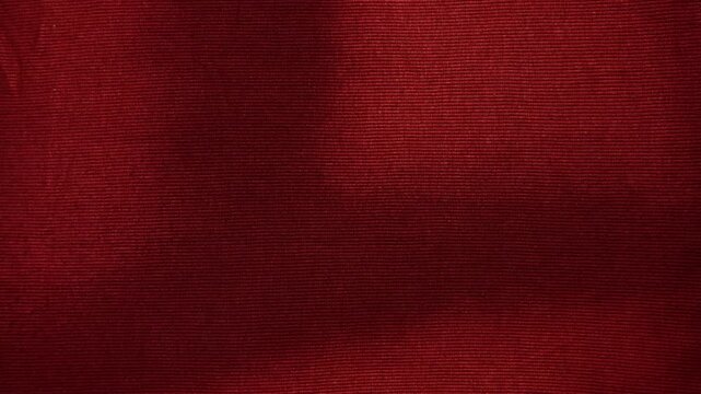 crimson red ribbed knit fabric texture moving gently under soft dramatic studio lighting creating subtle elegant shadows