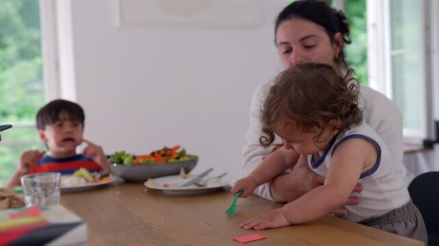 Mother removing toddler from dining table during family meal, highlighting gentle parenting, child safety and everyday family life