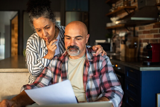 Senior couple reviewing bills on laptop at home kitchen