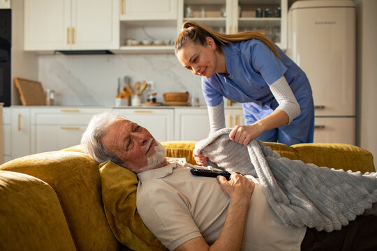 Caregiver covering sleeping senior on sofa at home