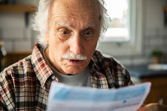 Senior man shocked by utility bill in home kitchen