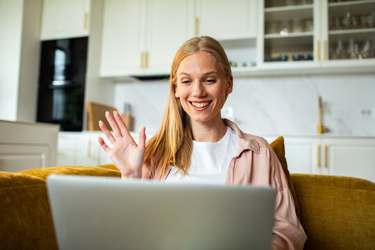 Smiling woman waving during video call in home kitchen