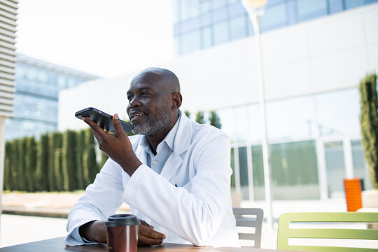 Doctor using smartphone voice assistant outside modern hospital campus
