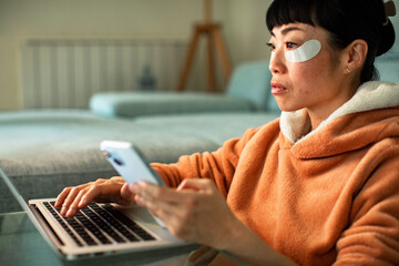 Woman working on laptop and phone at home with under-eye patches © Geber86