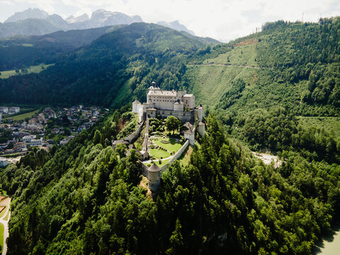 Aerial view of the historic Burg Hohenwerfen castle perched on a rocky hilltop surrounded by lush green forests and mountains in Werfen, Salzburg, Austria.