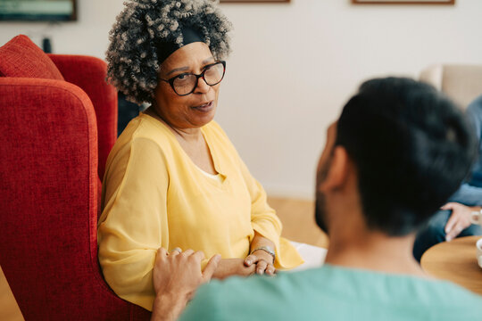 Senior woman talking to her male caregiver while sitting on armchair at retirement home
