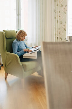 Retired senior woman spending leisure time reading book while sitting in armchair
