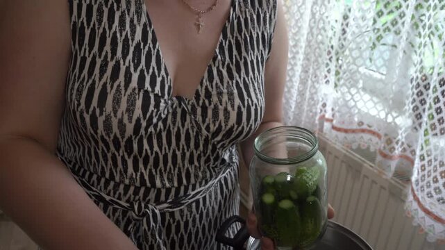 Woman putting fresh green cucumbers into glass jar close up, Housewife preparing organic vegetables for winter preservation