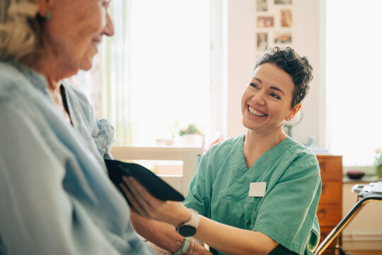 Female caregiver laughing while putting blood pressure cuff on elderly patient