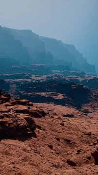 The sun shines on steep mountain cliffs above a dry, rocky desert. Shadows from the cliffs stretch out toward the horizon, creating a stark contrast against the bright sky.